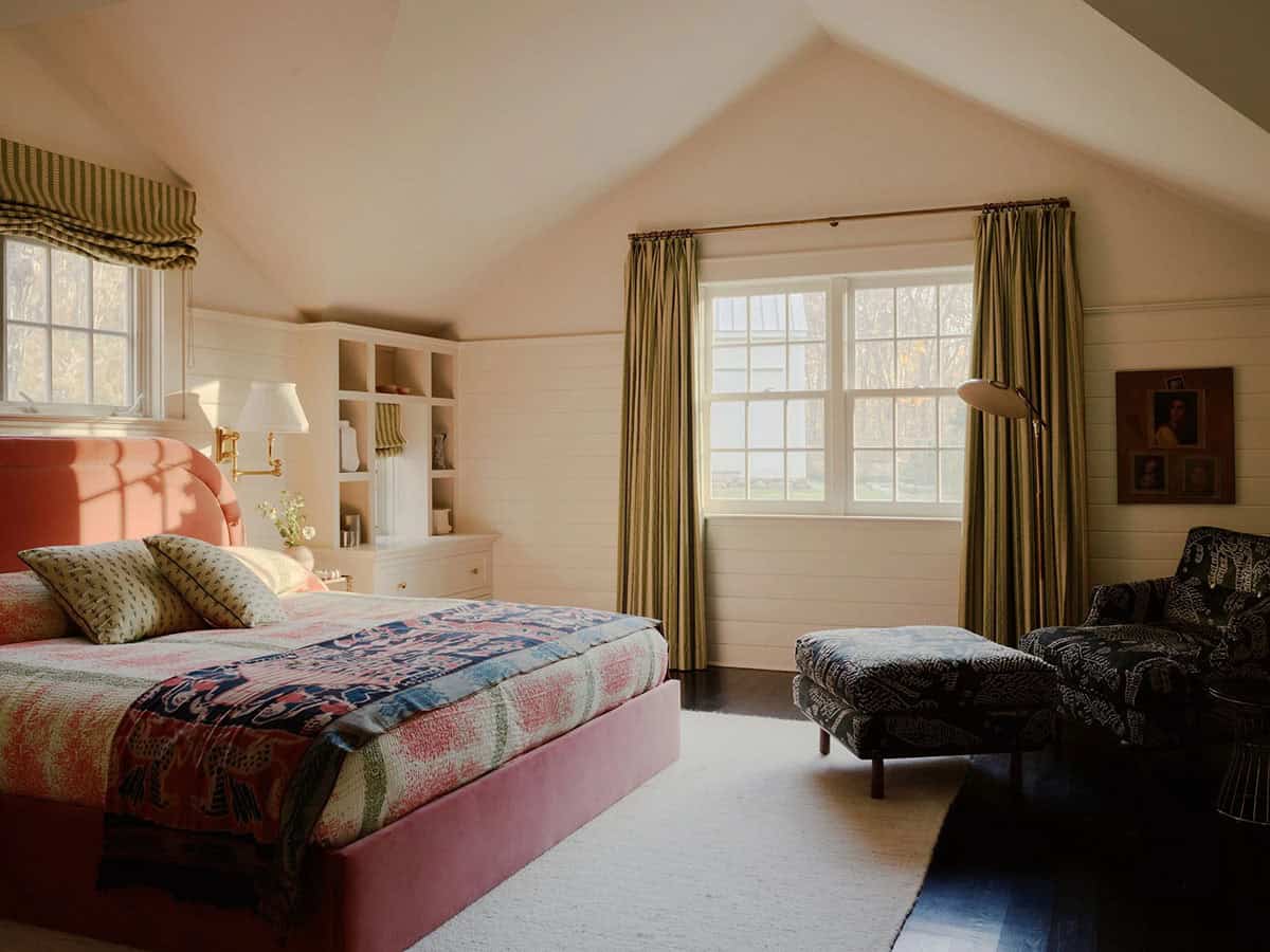 Attic bedroom with pink upholstered bed, striped curtains, and patterned chair