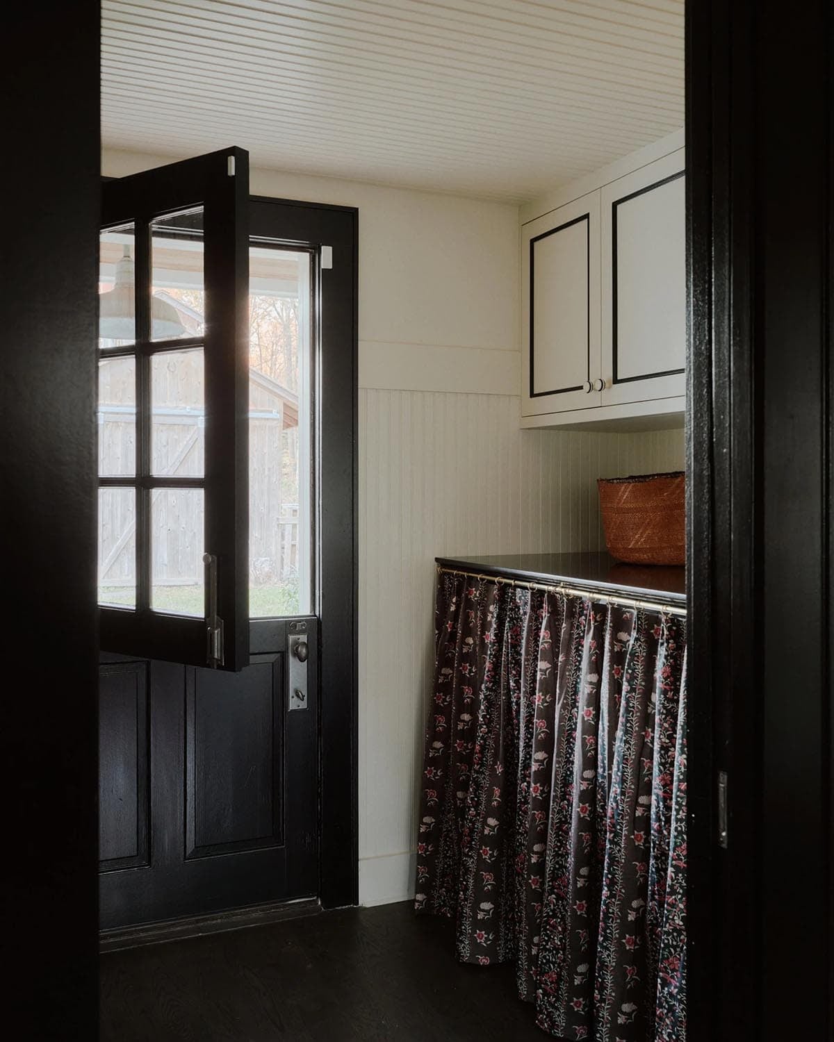 Mudroom with black Dutch door, floral curtain skirt, and beadboard cabinets