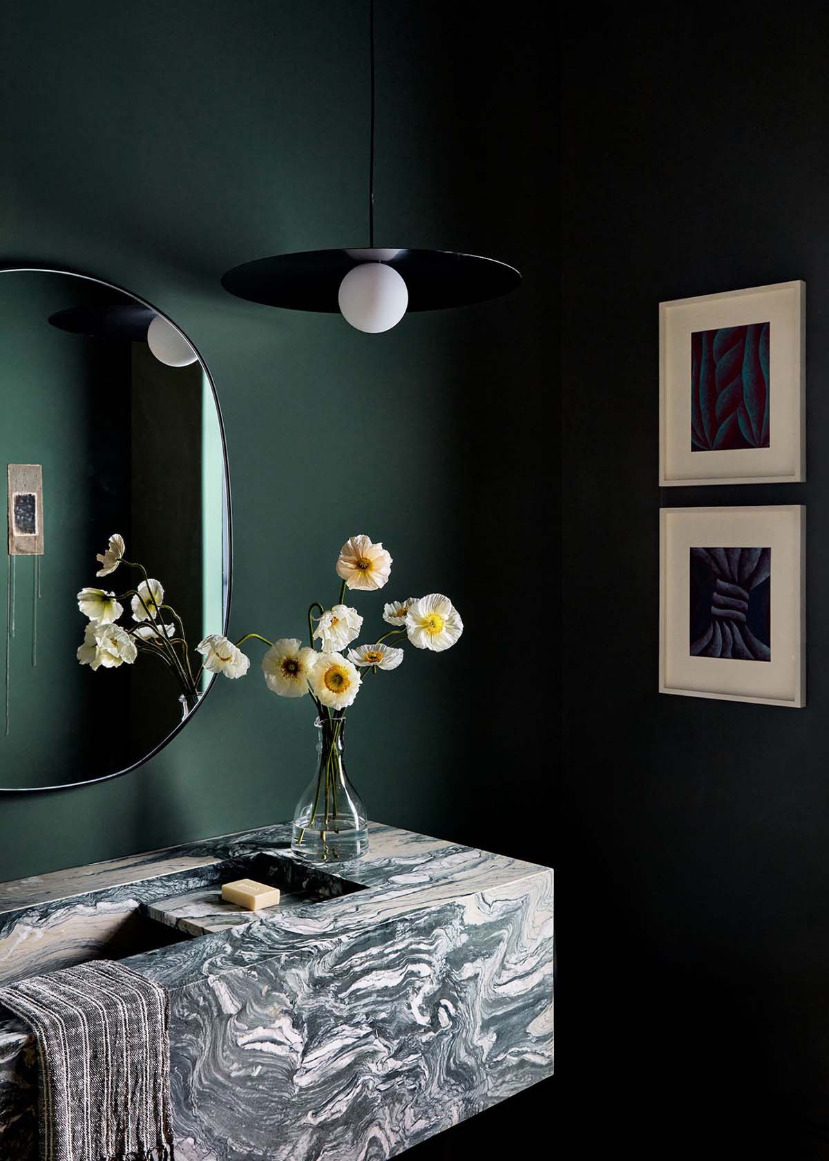 Moody green powder room with veined marble sink and floral mirror