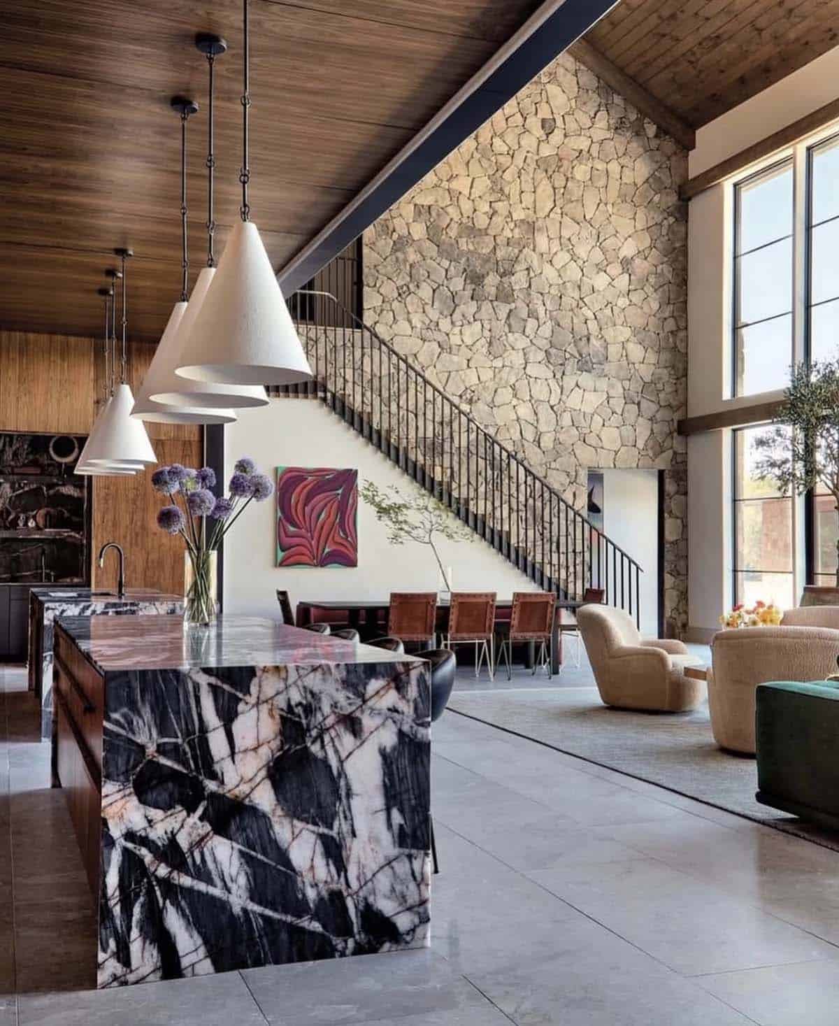 Open kitchen and dining area beneath dramatic stone staircase wall
