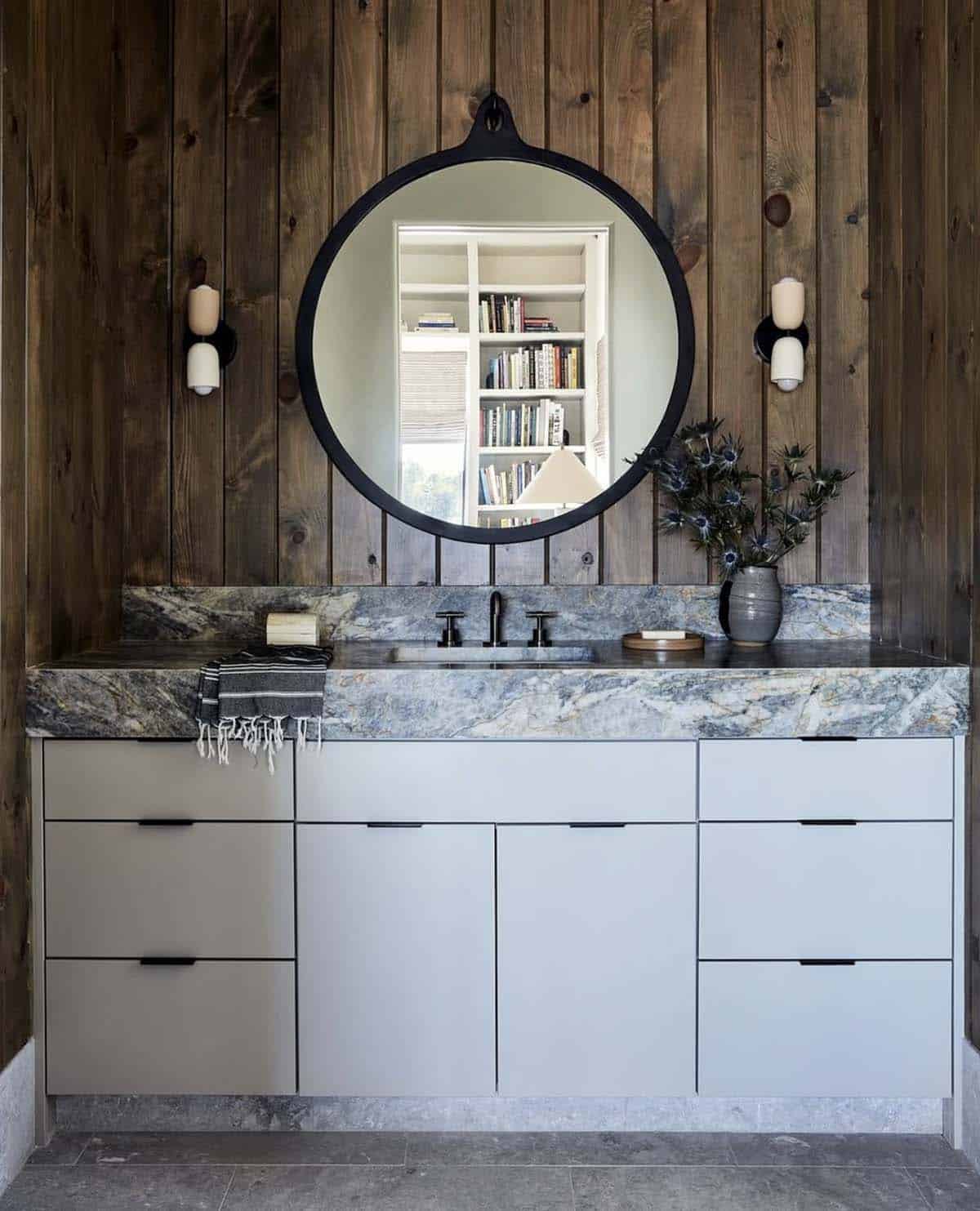 Wood paneled bathroom with round mirror and gray marble vanity
