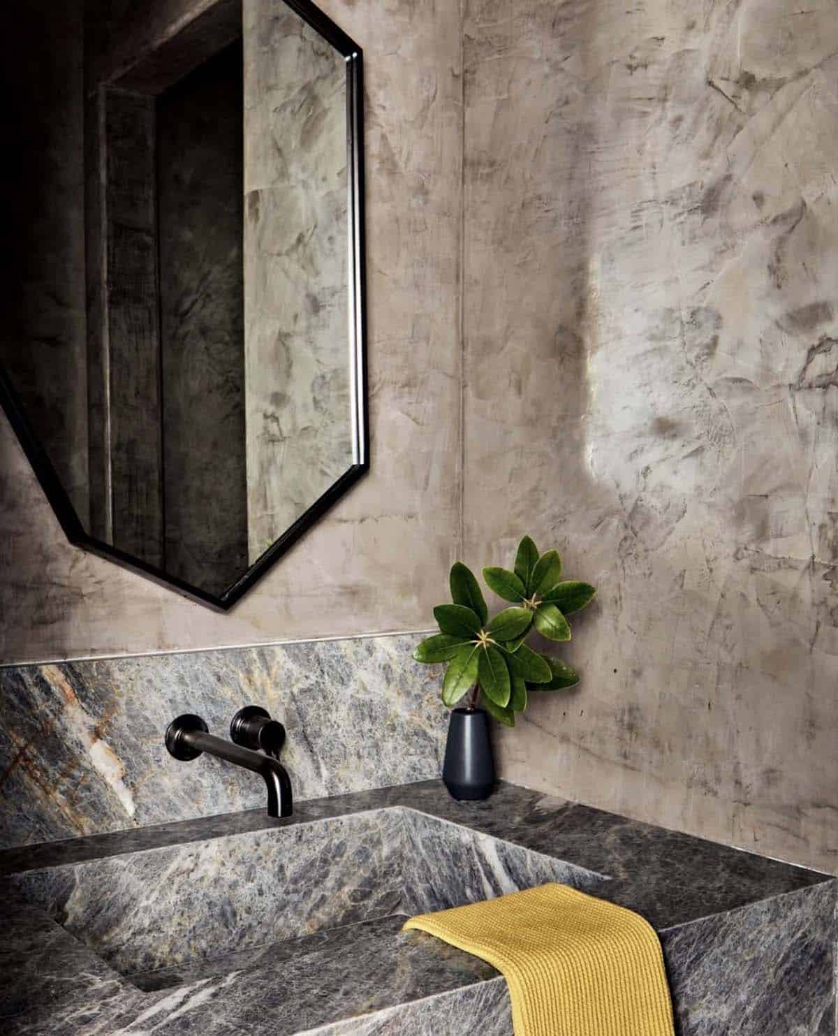 Marble powder room sink with black fixtures and hexagonal mirror