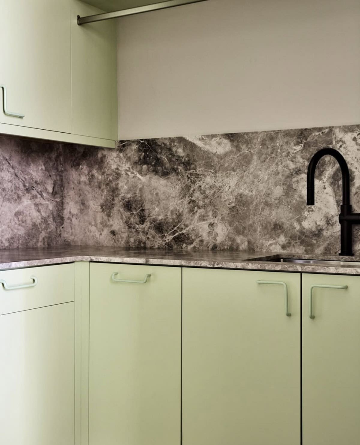 Sage green laundry room cabinets with gray marble backsplash and sink