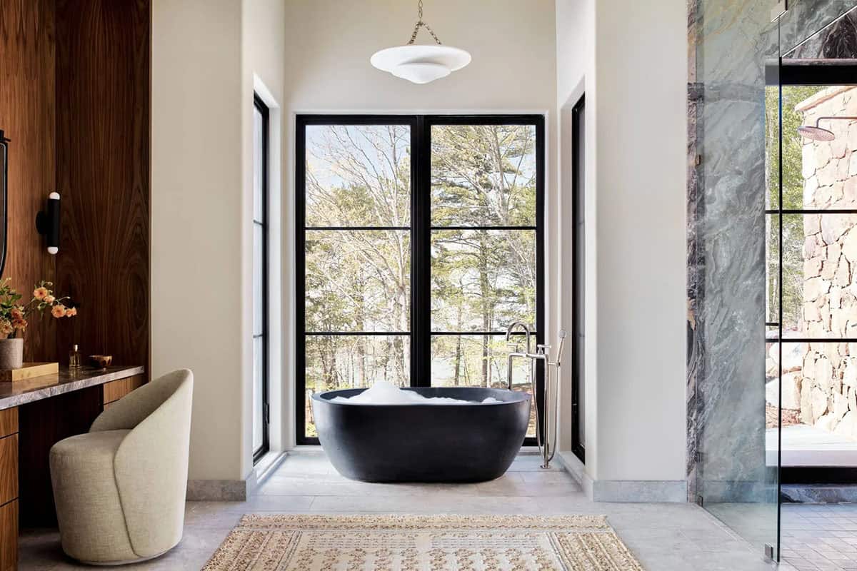 Primary bathroom with black soaking tub facing forest view windows