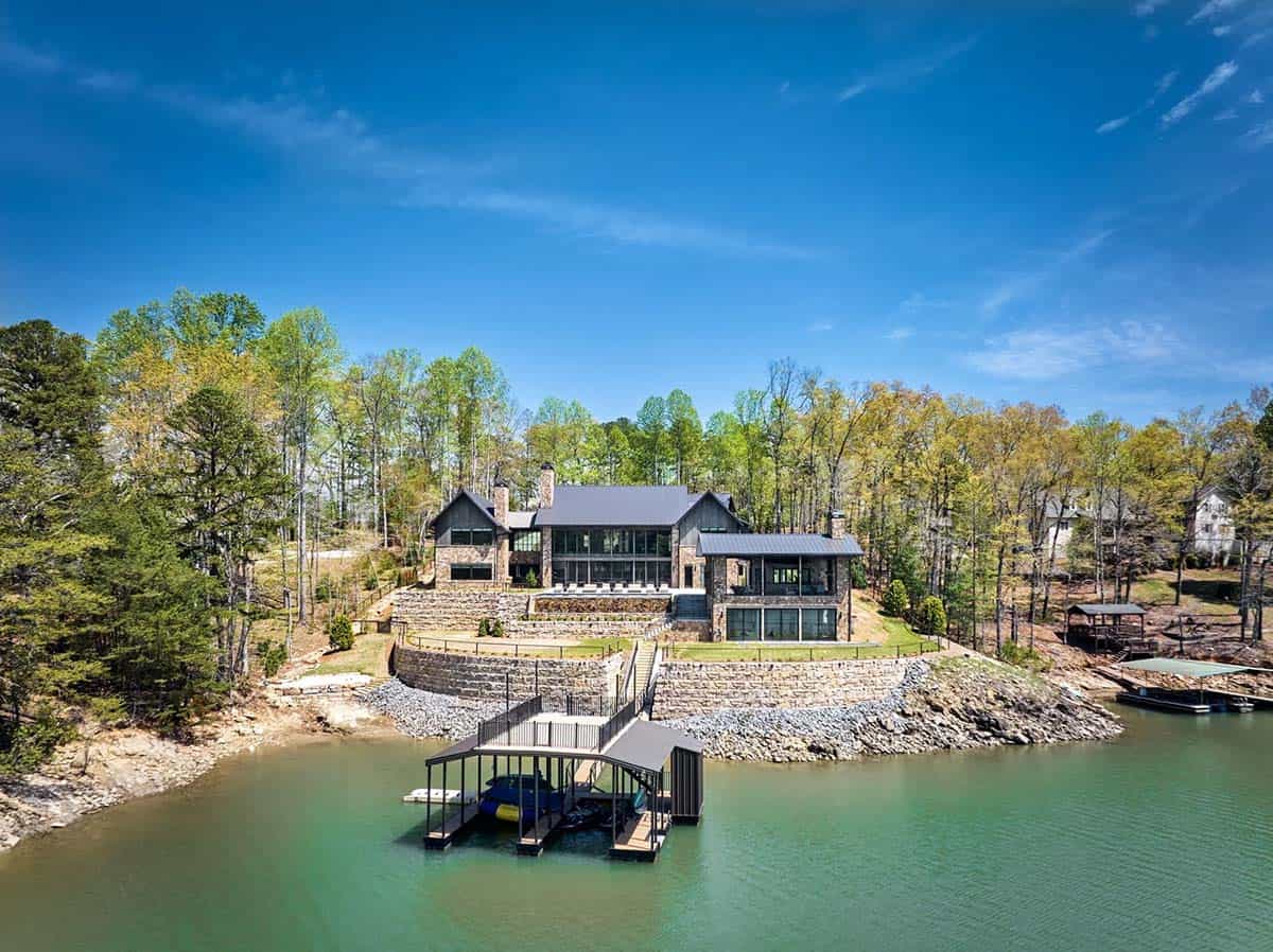 Aerial view of lakefront home with covered boat dock and stone seawall