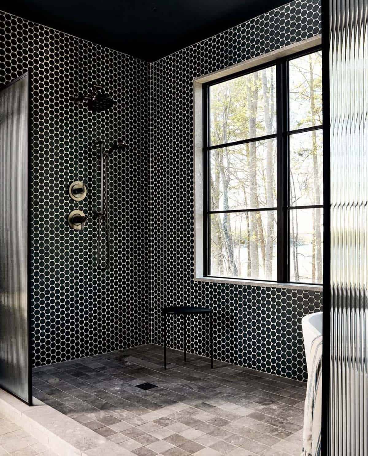Black penny tile shower with brass fixtures and forest view window
