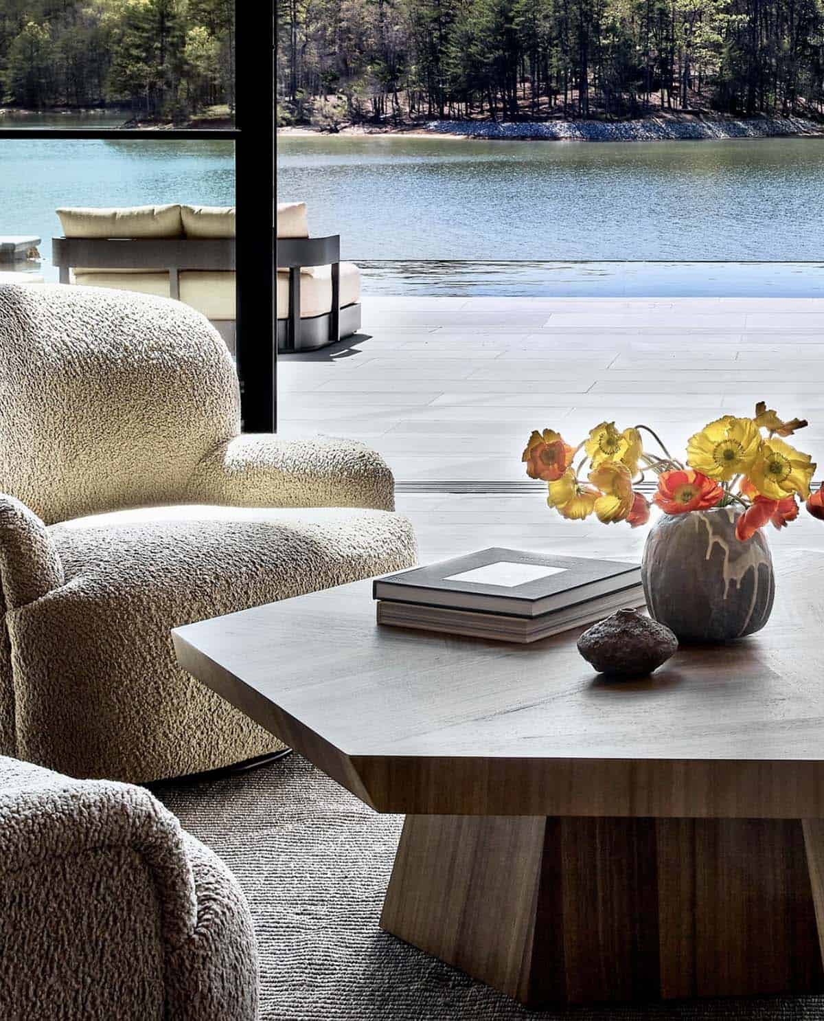 Boucle armchair beside coffee table with lake and pool view beyond