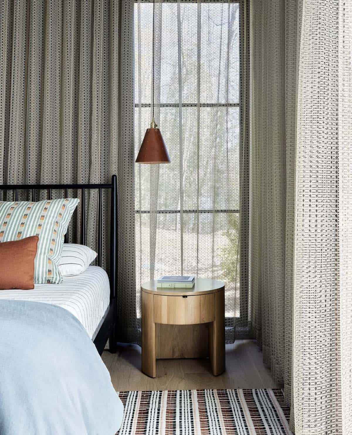 Round wood nightstand with leather cone pendant light beside sheer curtains