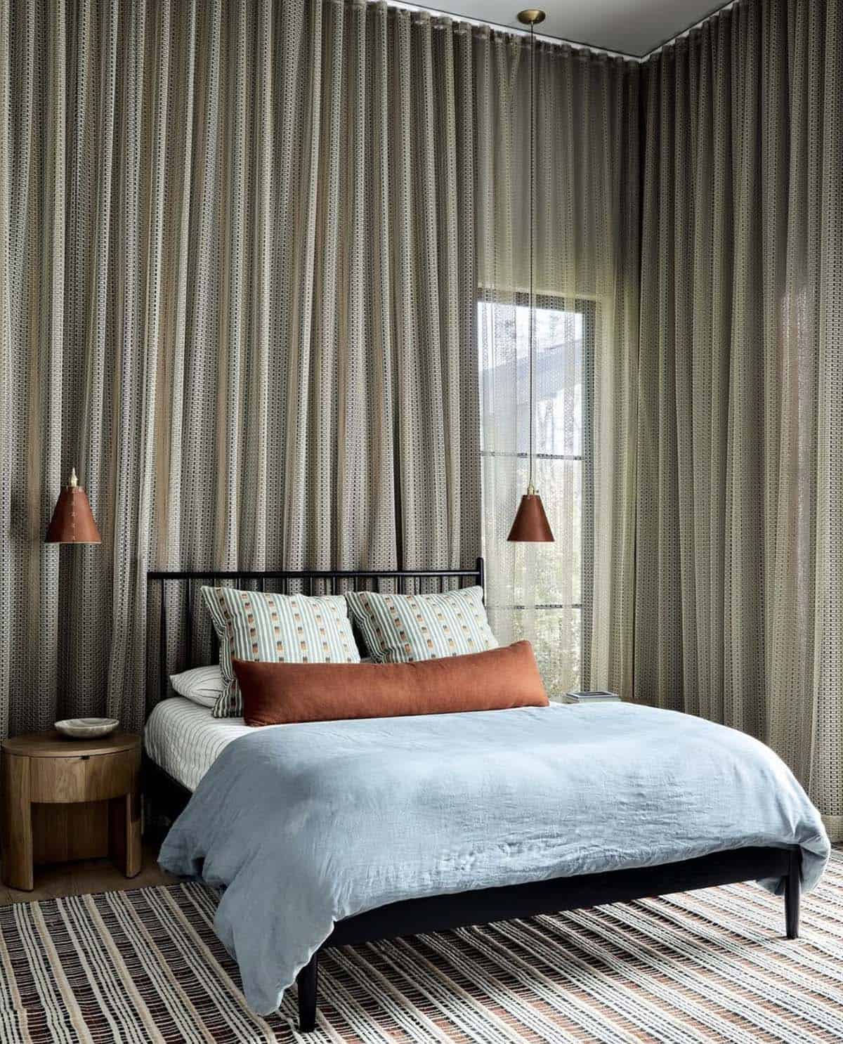 Guest bedroom with sheer draped walls and black metal bed frame with blue linens