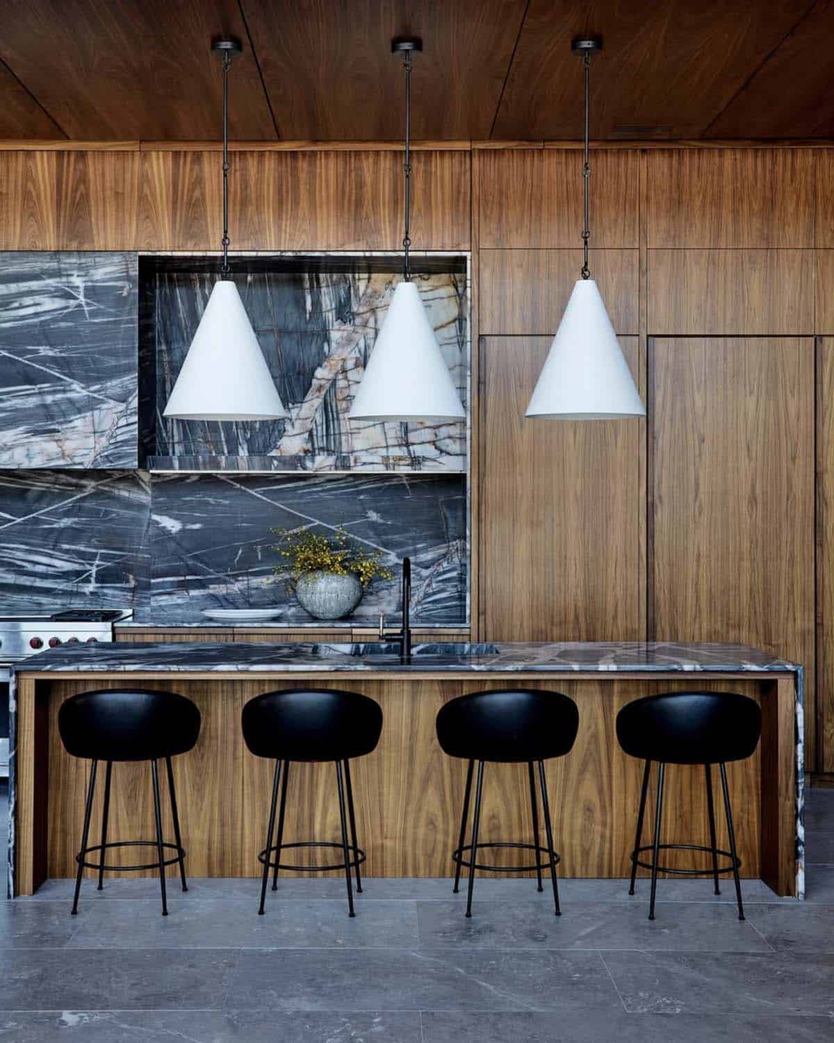 Kitchen island with black stools and cone pendants beneath quartzite backsplash
