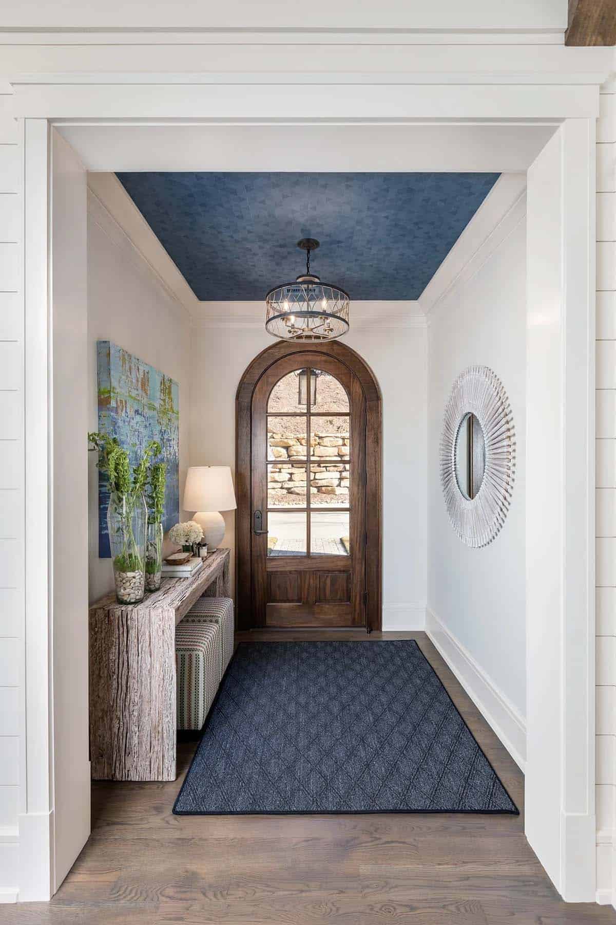 Entryway with arched wood door, patterned blue ceiling, and rustic console table