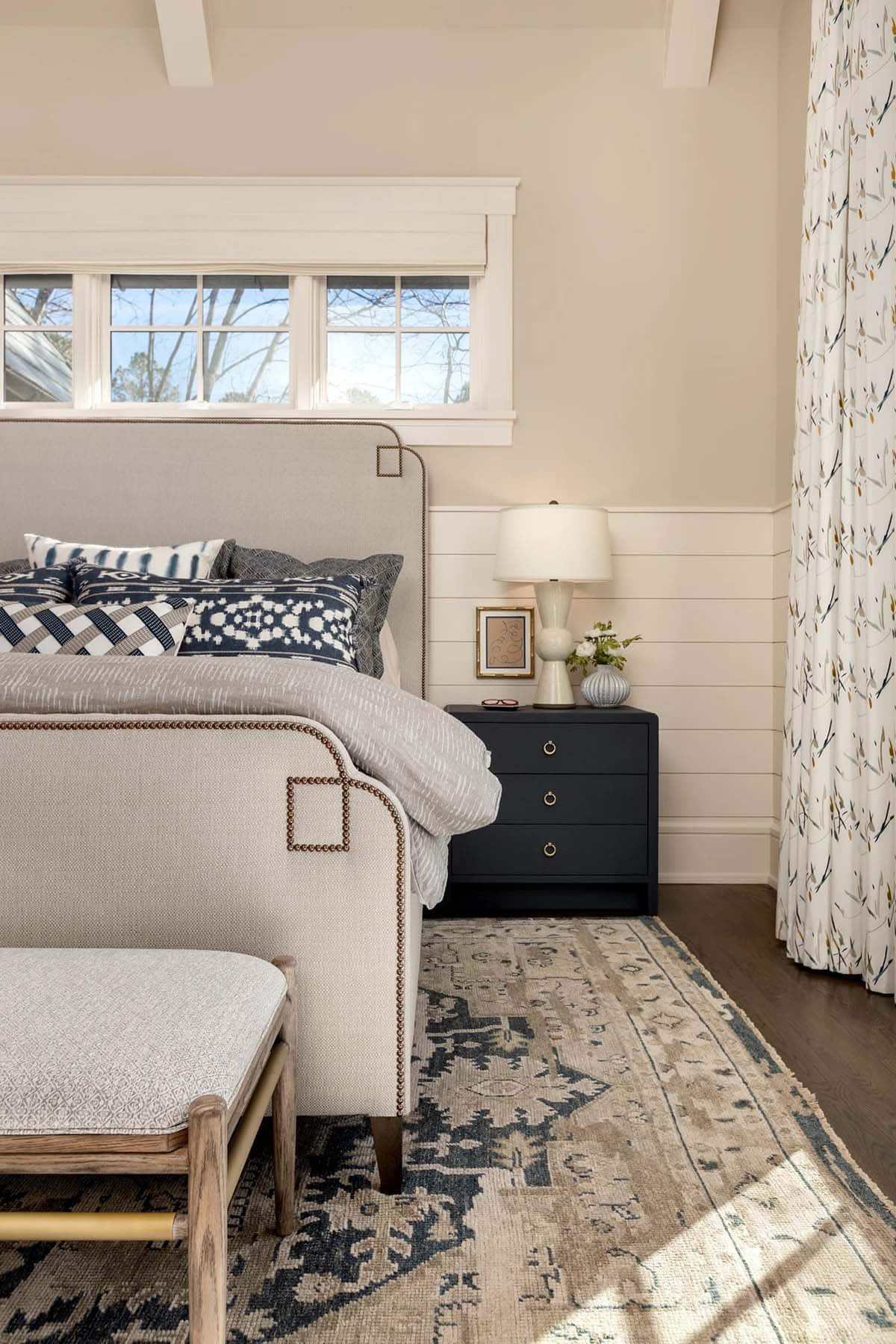 Close-up of upholstered bed with navy patterned pillows and dark nightstand