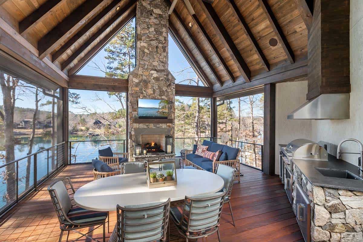 Screened porch with stone fireplace, dining table, and outdoor kitchen overlooking lake