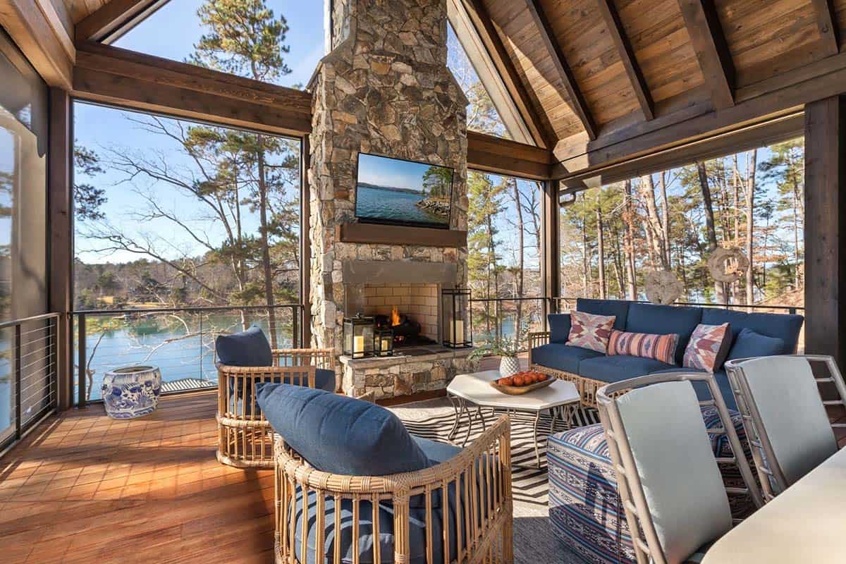Screened porch seating area with stone fireplace and wicker furniture facing lake