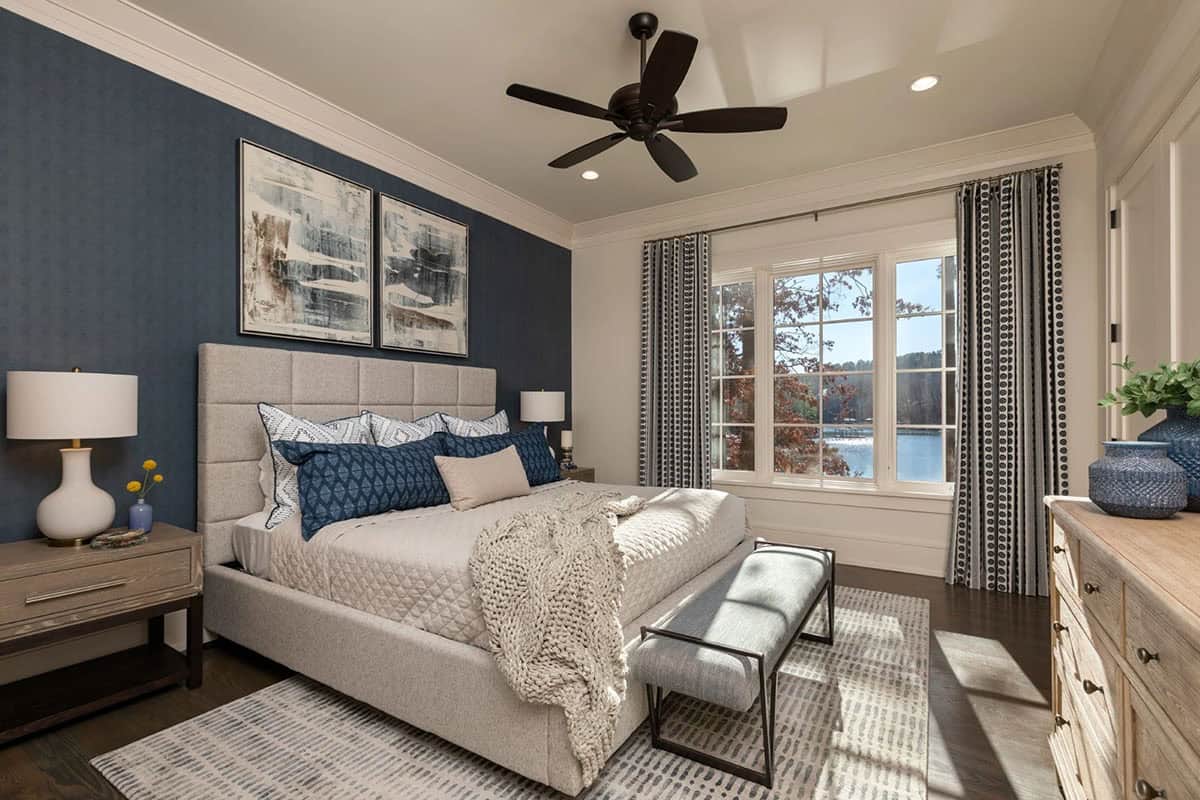 Bedroom with navy accent wall, upholstered headboard, and lake-view window