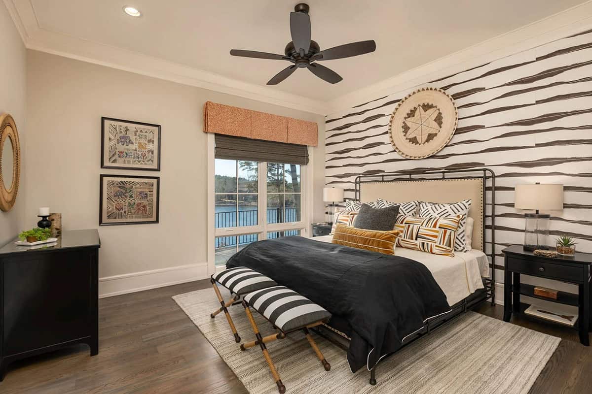 Bedroom with striped wallpaper, black metal bed frame, and lake-view balcony