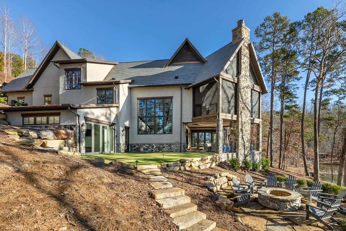 Rear exterior of stone and stucco home with putting green, fire pit, and Adirondack chairs
