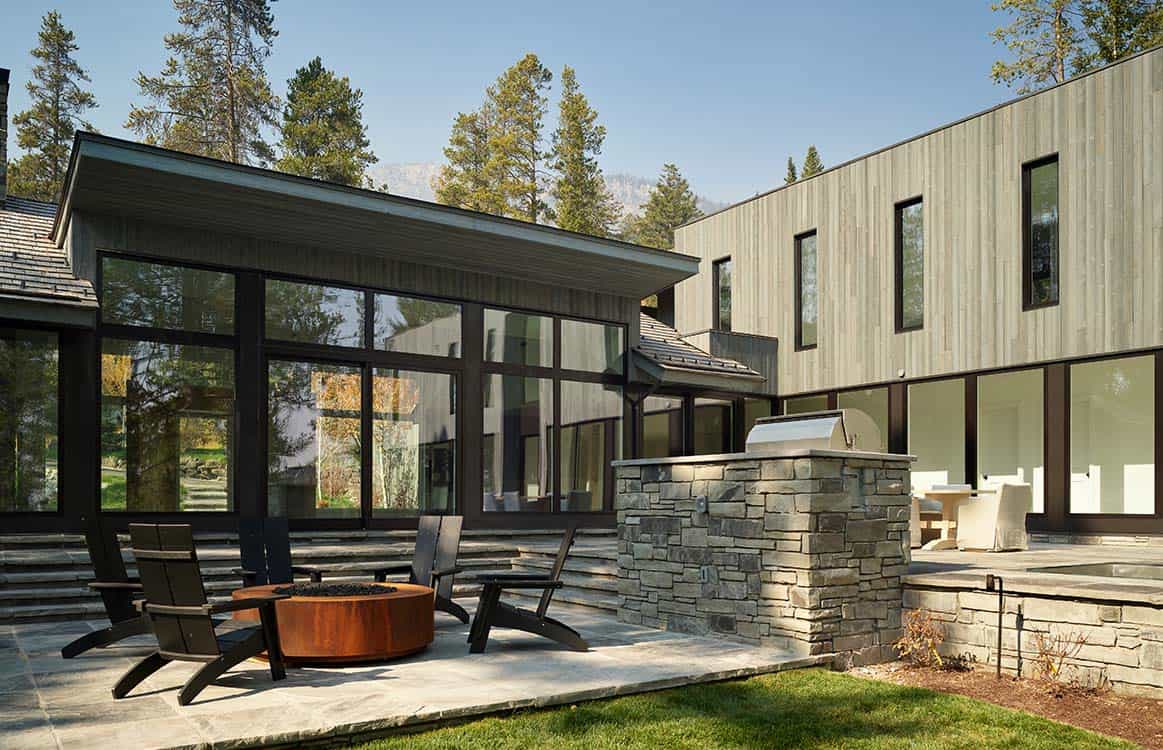 Patio seating area with fire pit beside stone outdoor kitchen and wood-clad two-story addition