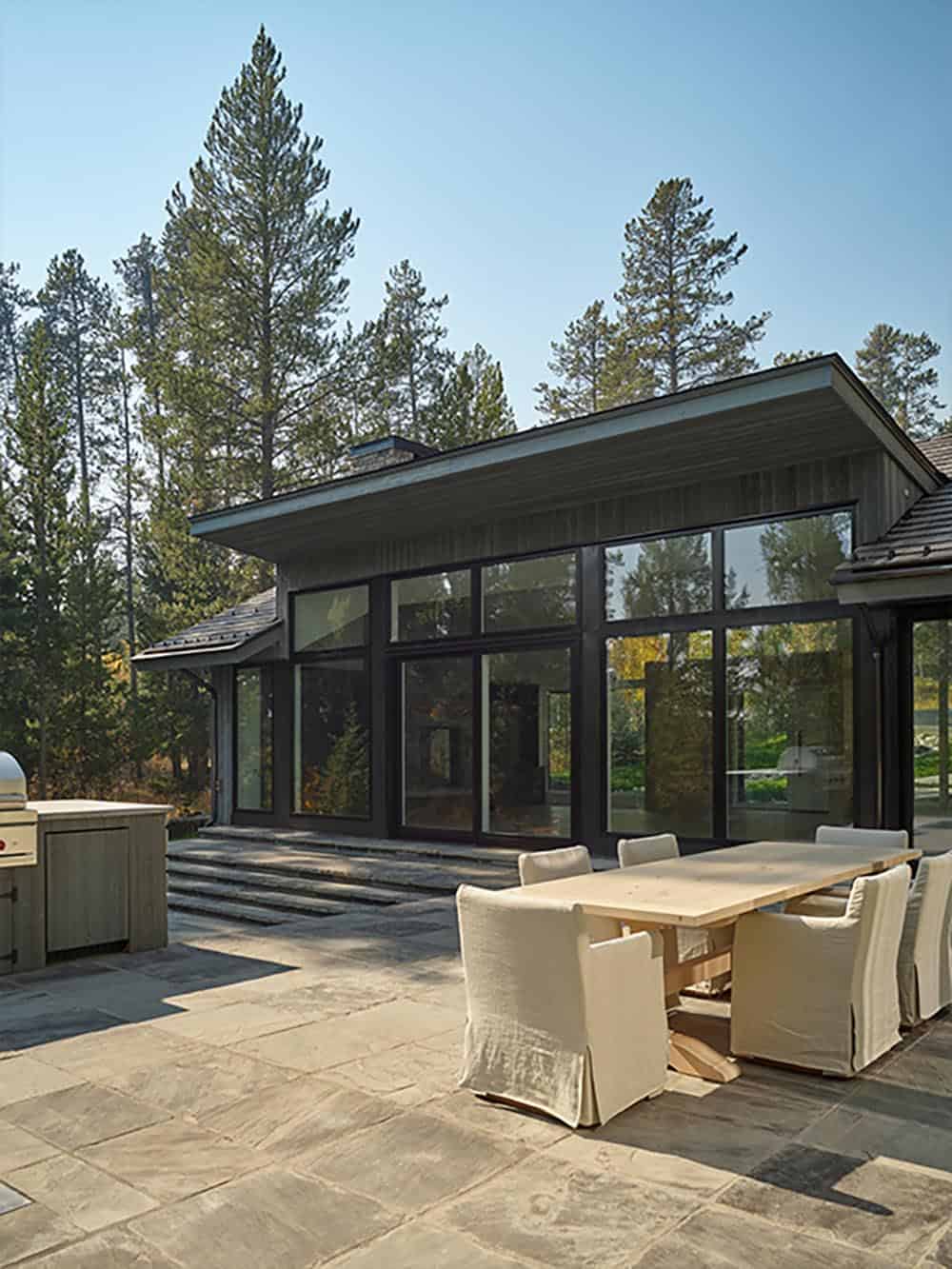 Stone patio with outdoor dining table and built-in grill beneath the home's deep roof overhang