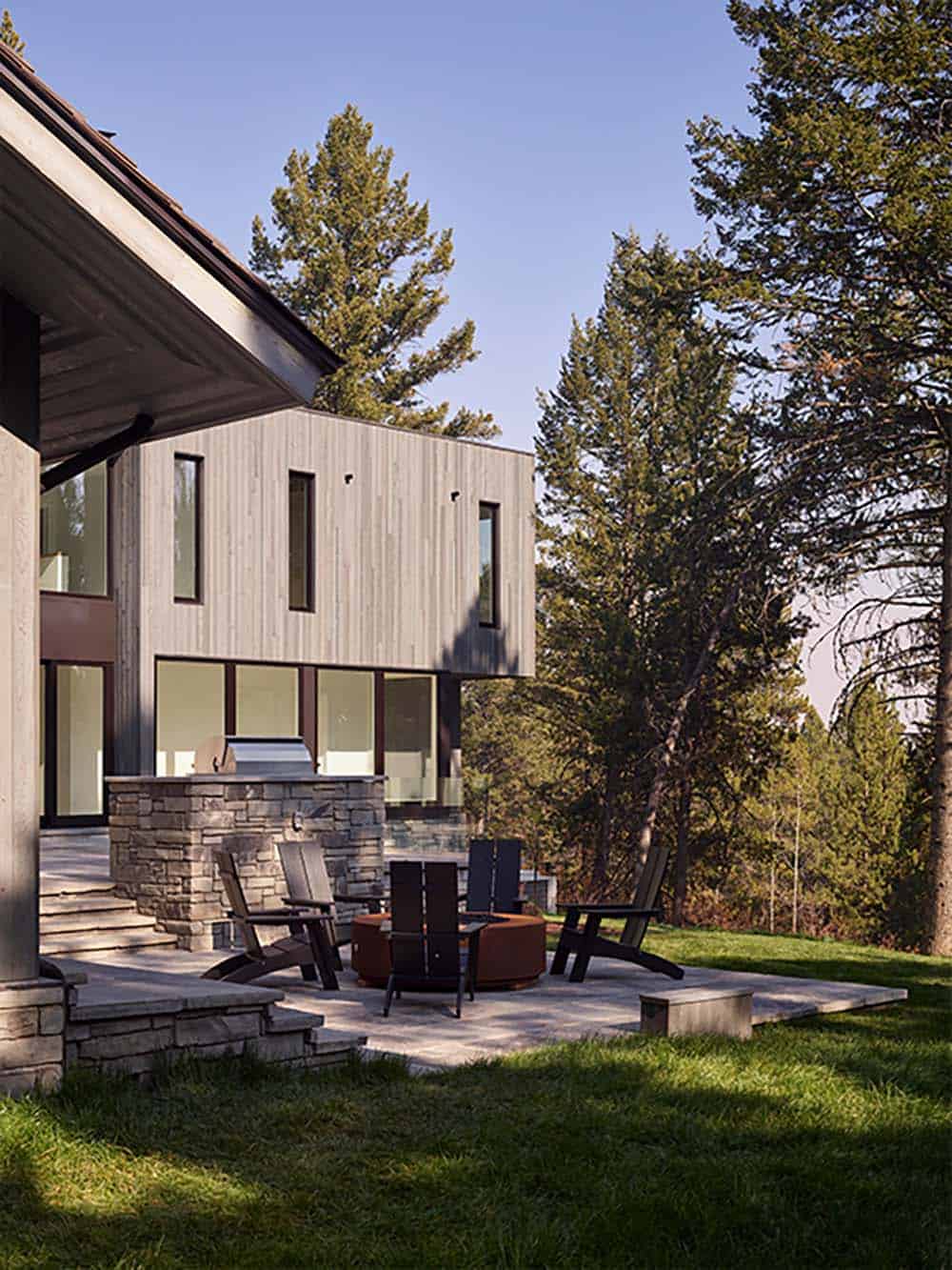 Fire pit lounge area with Adirondack chairs beneath cantilevered wood-clad upper level