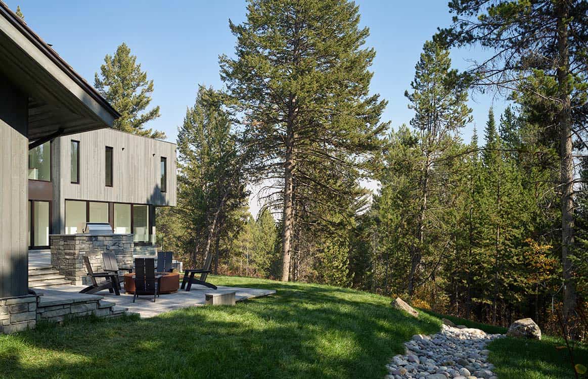 View across sloped lawn toward the home's wood siding and outdoor fire pit patio