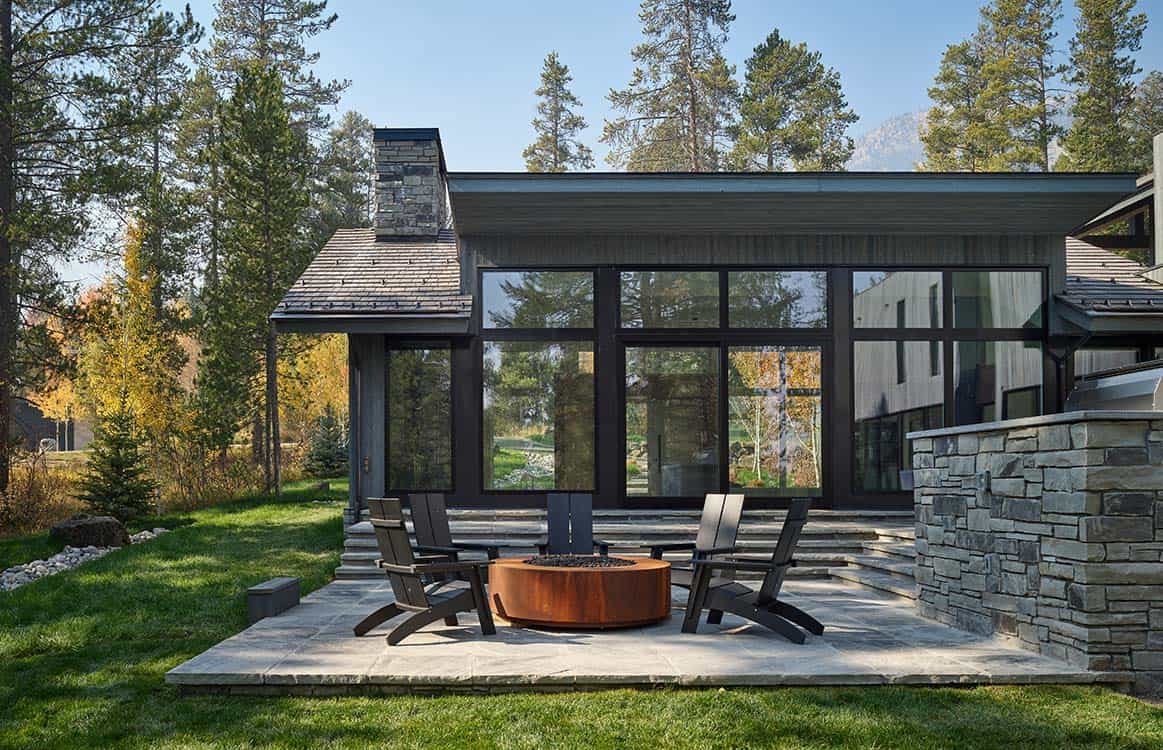 Corner patio with fire pit and stone chimney facing the surrounding pine forest
