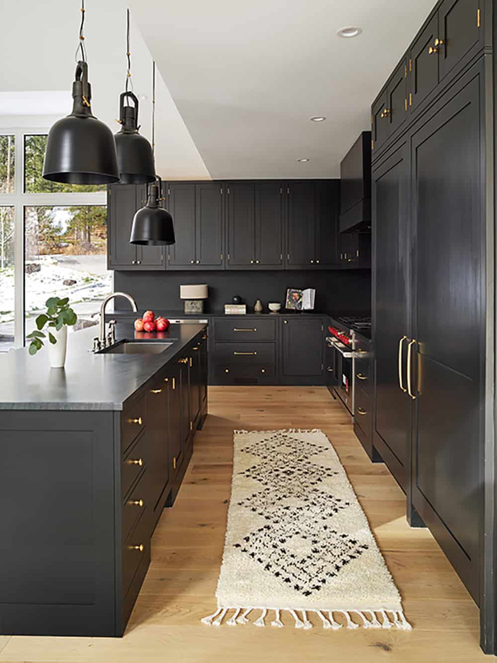Black kitchen cabinetry with brass hardware, black pendant lights, and patterned runner rug