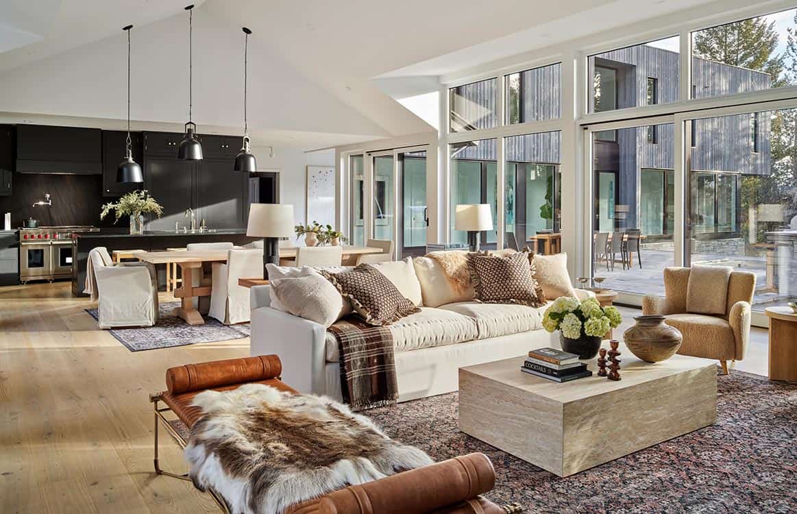 Great room with layered rugs, leather bench, and wall of windows overlooking the deck