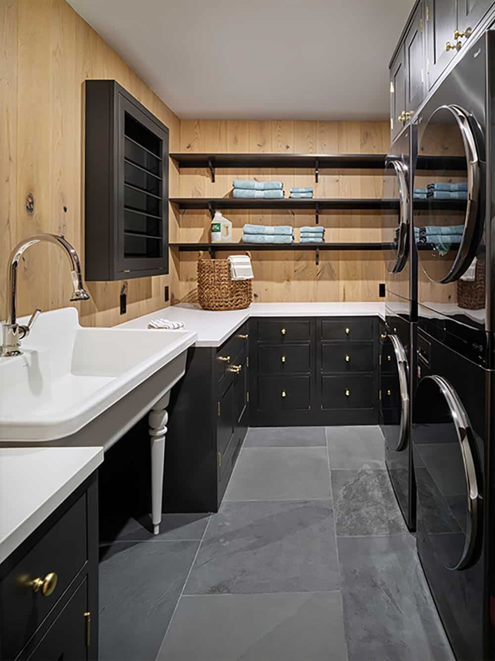 Laundry room with black cabinetry, stacked washer/dryer, and farmhouse sink