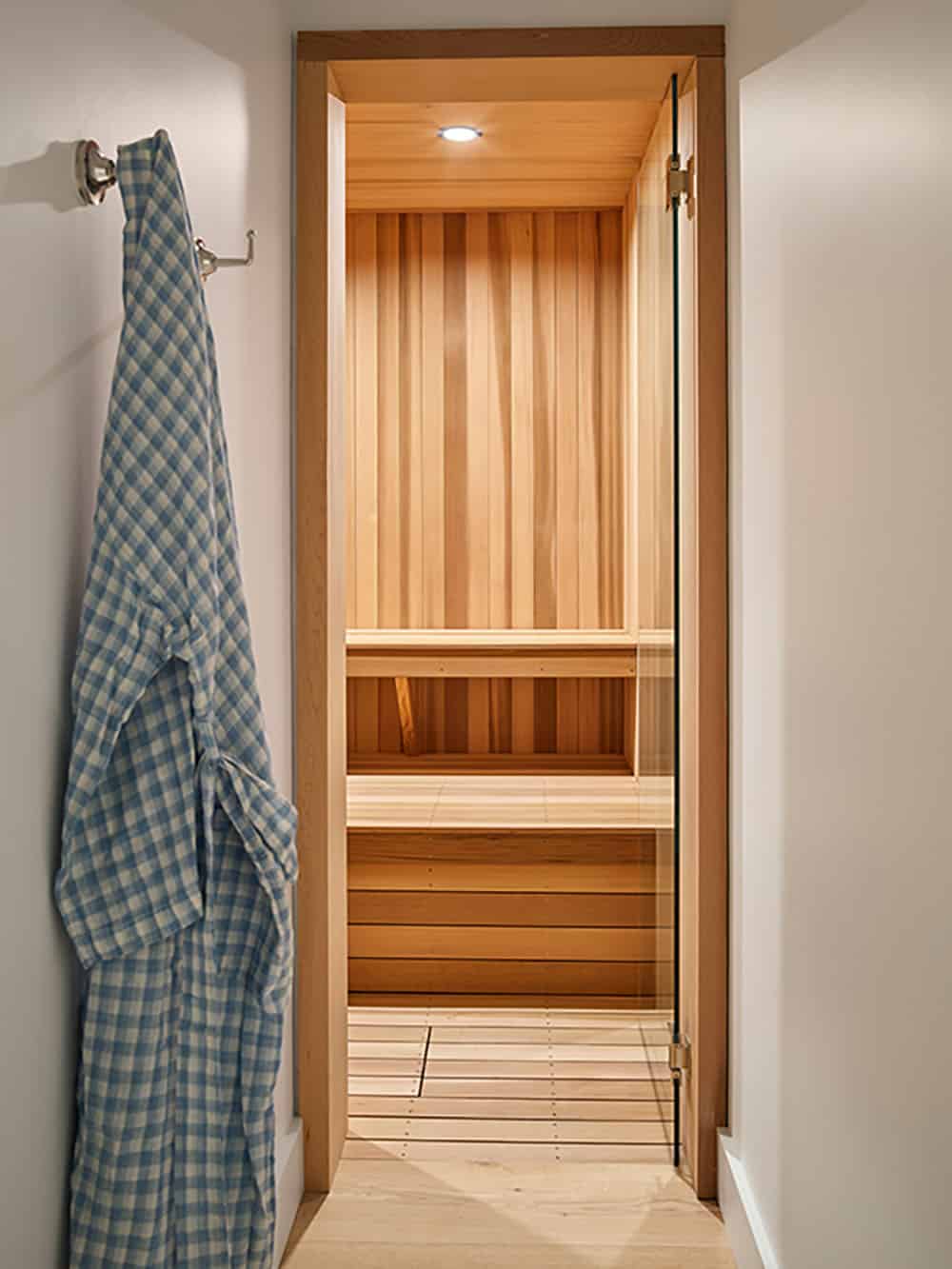 Cedar-lined home sauna viewed through glass door with robe hanging beside it
