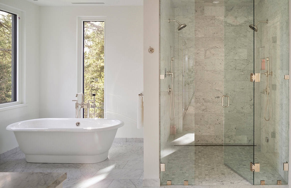 Freestanding soaking tub beside a glass-enclosed marble tile shower