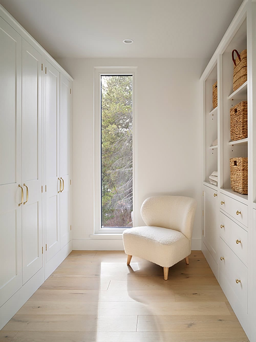 White walk-in closet with paneled cabinetry, woven storage baskets, and a boucle accent chair