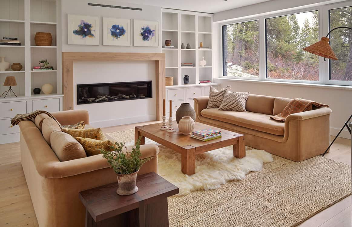 Living room with tan velvet sofas, linear fireplace, and blue floral artwork above white built-ins