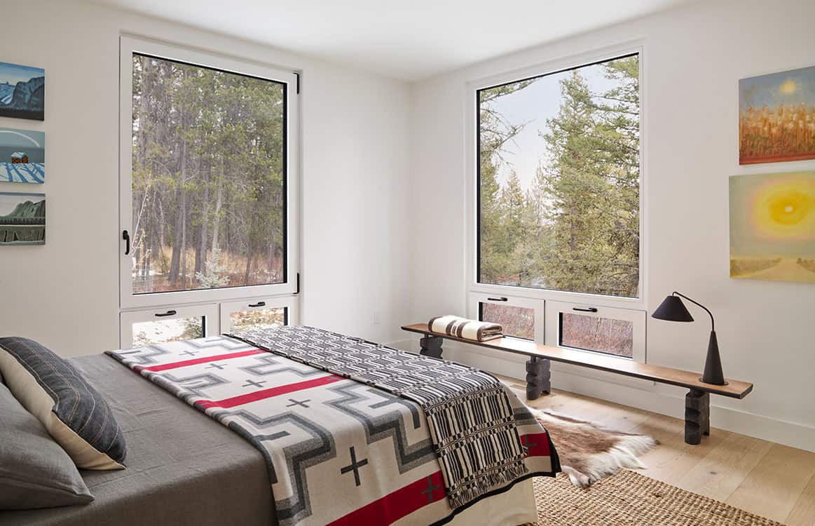 Bedroom with patterned wool blanket, corner windows, and wood bench beneath the sill
