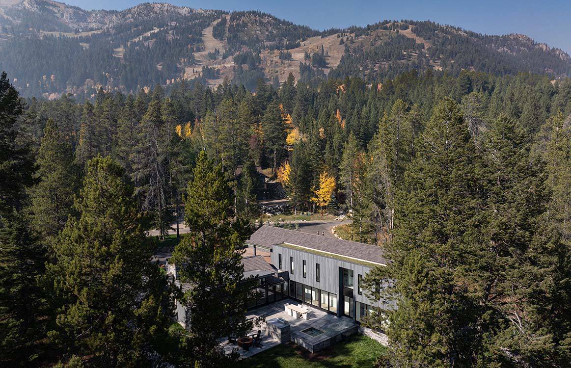 Aerial view of the mountain home nestled in pine forest with ski slopes visible in the distance