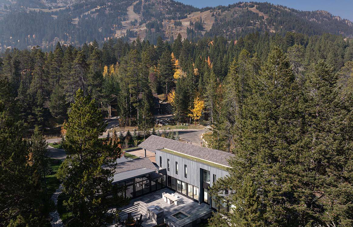 Aerial shot of the residence framed by evergreens with a ski hill rising beyond the treeline
