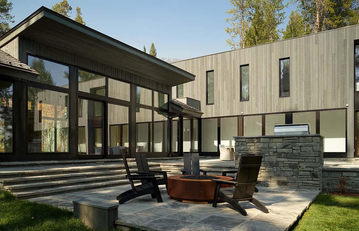 Patio with fire pit and Adirondack chairs framed by the home's glass walls and wood siding