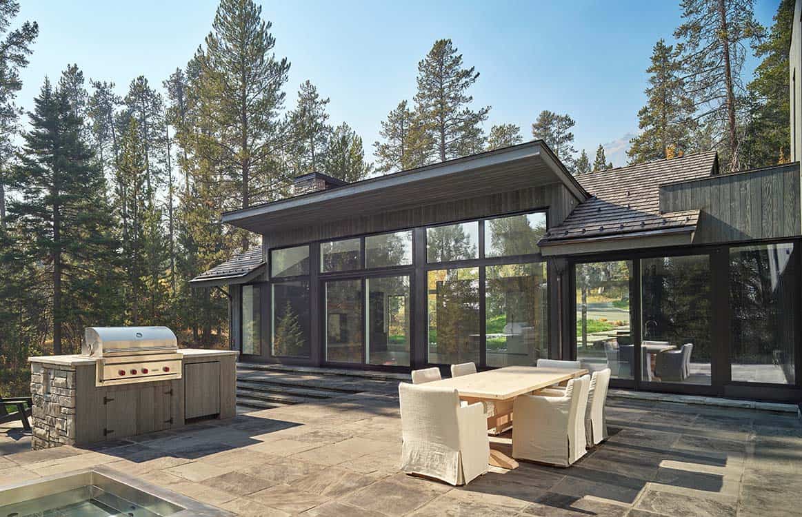 Outdoor dining terrace with stone kitchen and grill overlooking the wooded property