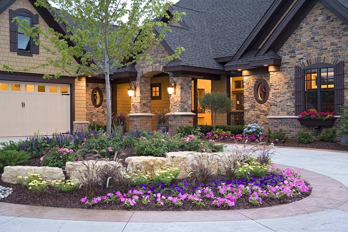 Stone and shingle luxury home exterior with circular flower bed and three-car garage
