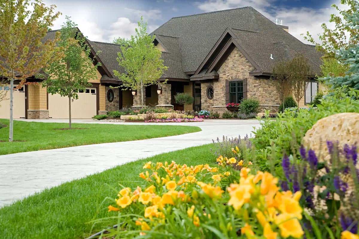 Front view of custom stone home with manicured lawn and flower beds