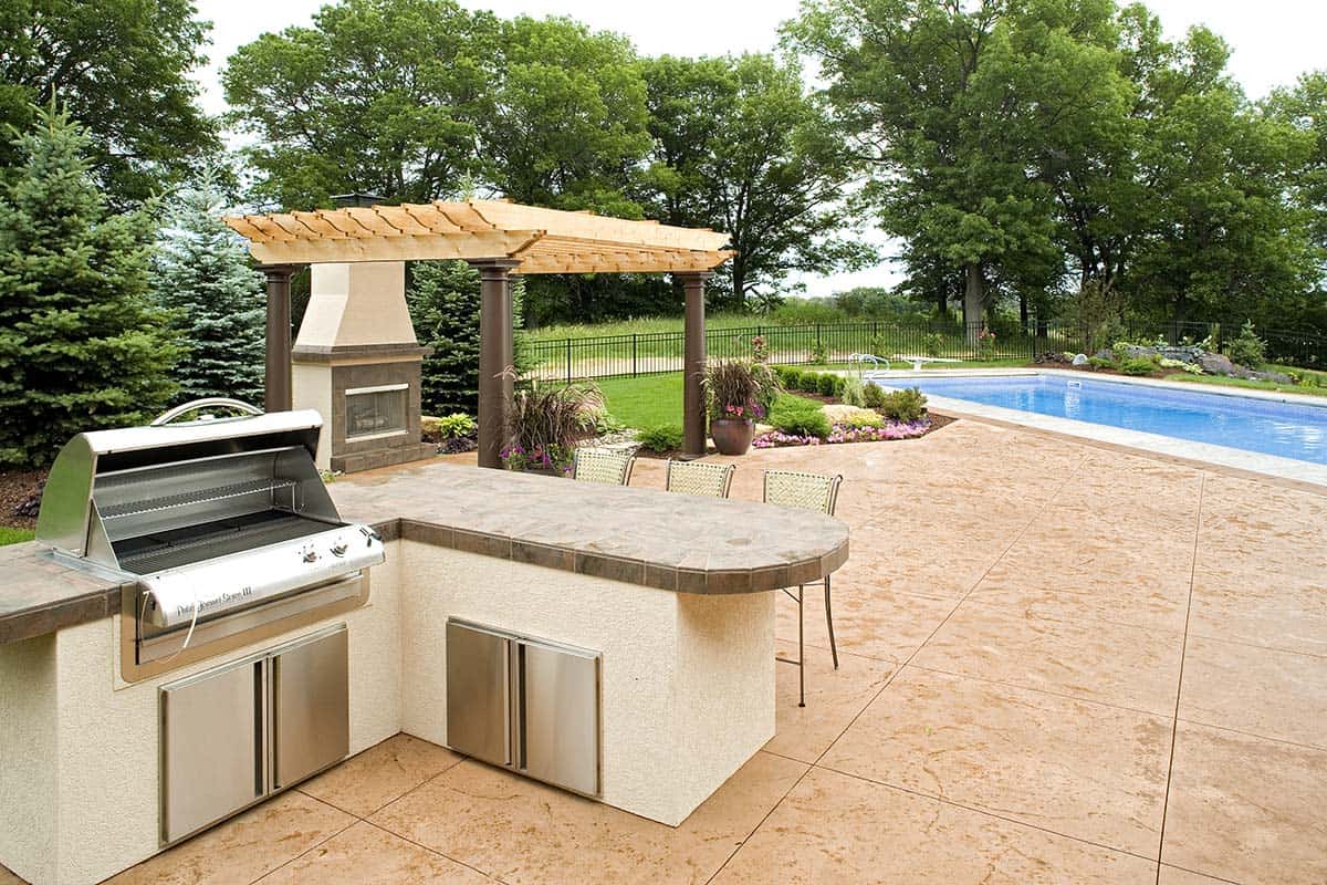 Outdoor kitchen with built-in grill overlooking pool and pergola