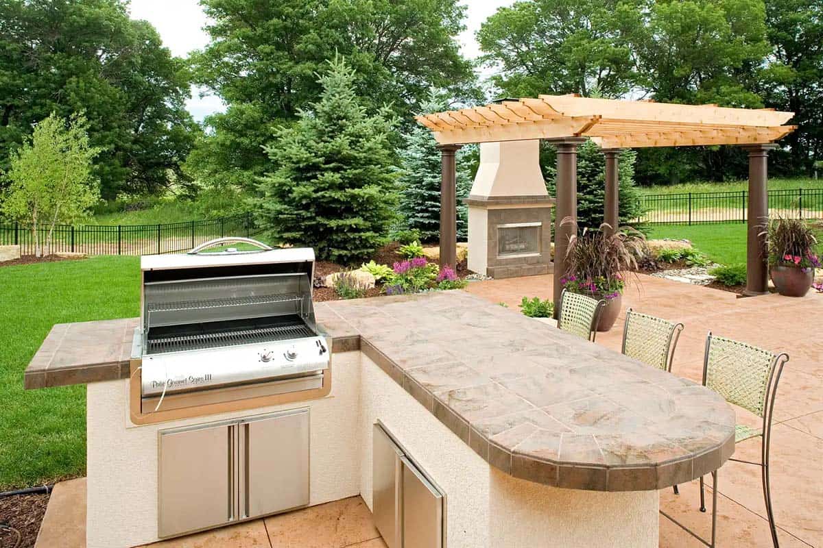 Built-in outdoor grill and stone countertop bar with pergola in background