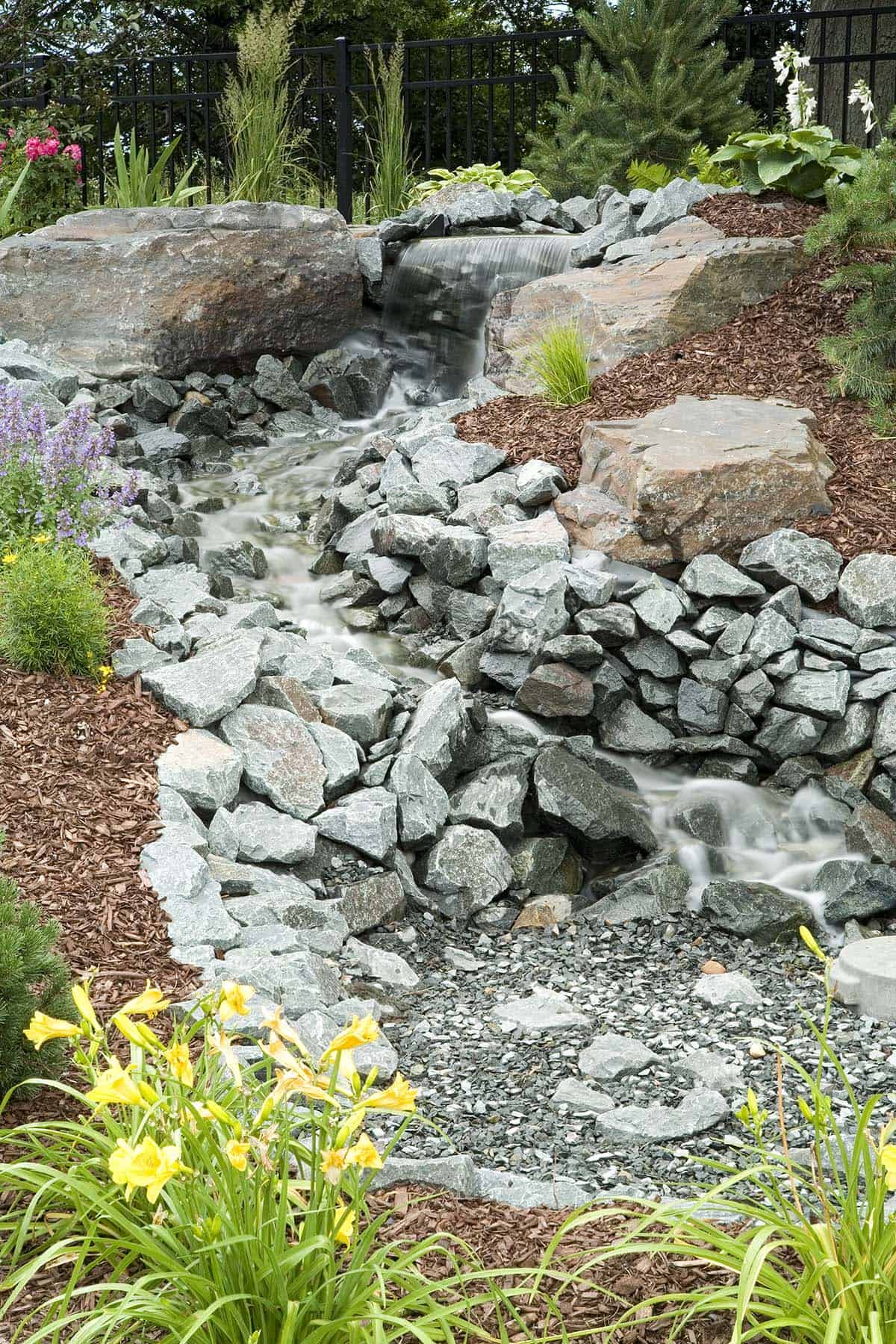 Rock waterfall feature with daylilies and perennial garden beds