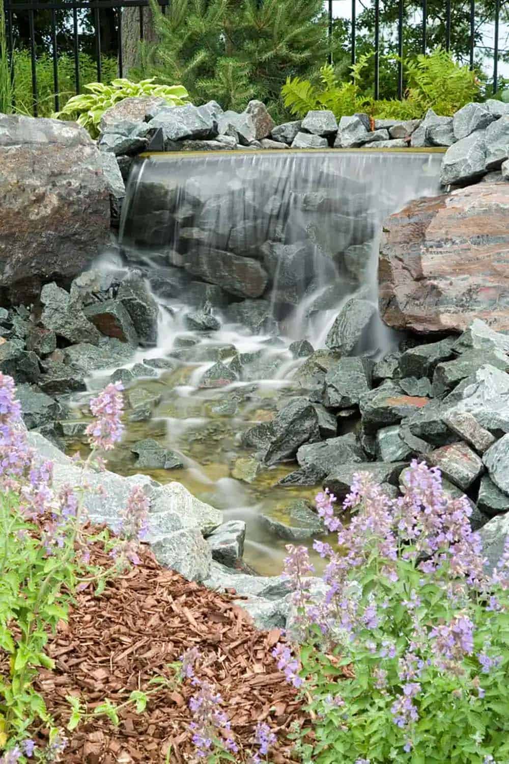 Stone waterfall cascading into small pond surrounded by catmint