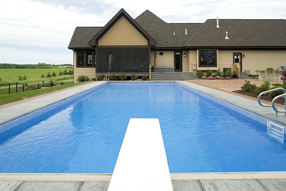 Rectangular swimming pool with diving board facing rear of home