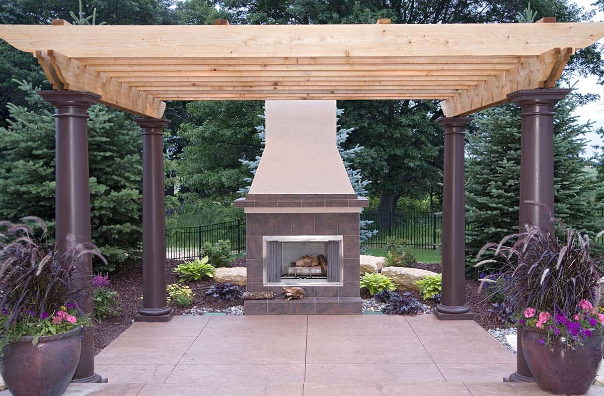 Stone outdoor fireplace centered beneath wooden pergola with round columns