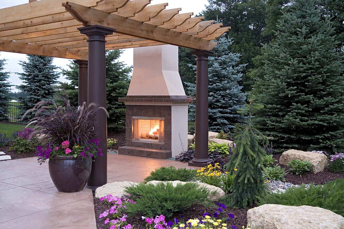 Outdoor stone fireplace beneath cedar pergola with potted flowers