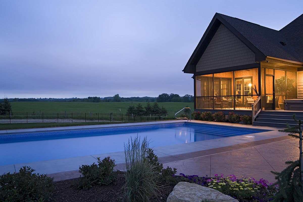 Backyard pool with screened porch and open field view at dusk
