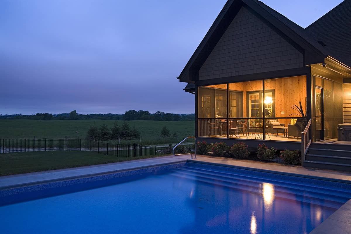 Rectangular pool and lit screened porch under evening sky