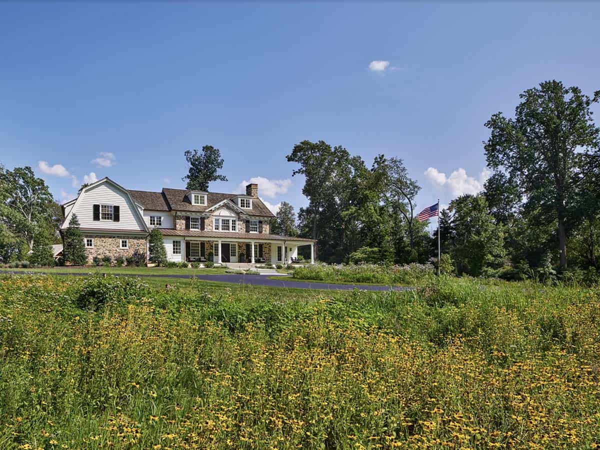 Farmhouse exterior viewed from the driveway, framed by mature trees and tall grasses